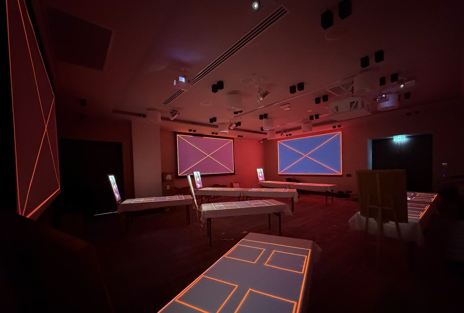 A banquet room in the dark during calibration: alignment frames on the screens and amber outlines on every table