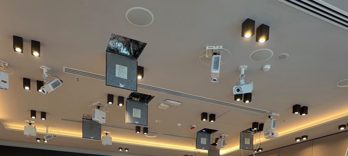 A ballroom ceiling during an installation: projectors on their mounts between the downlights