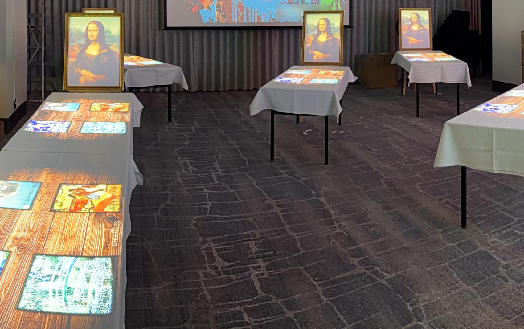 The same room with the work lights on: tables carrying projected content during the build