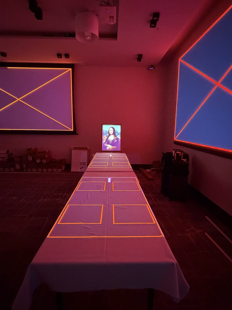 A long table during calibration, amber frames projected onto the cloth where the plates will stand